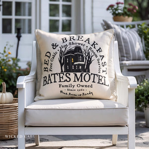 Decorative pillow with 'Bates Motel' design on a white chair outdoors.