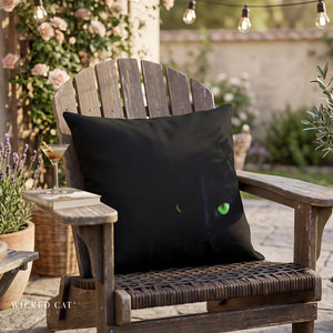 Green cat eyes on a black pillow on an outdoor chair with a dirty martini on a book.