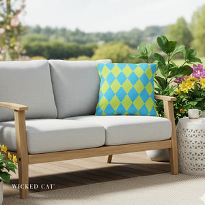 Gray outdoor sofa with a blue and green diamond pattern pillow on a wooden deck with plants and flowers.