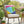 Wicker chair with a colorful geometric pillow on a patio with plants and flowers.