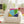 Colorful geometric pillow on a white chair in a child-friendly room with toys and plants.