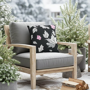 Outdoor chair with gray cushions and a floral pillow, surrounded by potted plants and firewood.