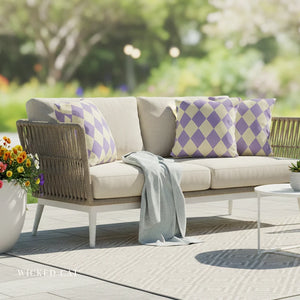 Outdoor patio set with a beige sofa, patterned cushions, and a small table with flowers on a wooden deck.
