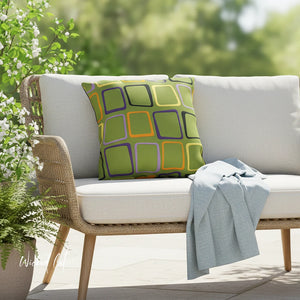 Outdoor sofa with a colorful pillow and a blanket, surrounded by greenery.