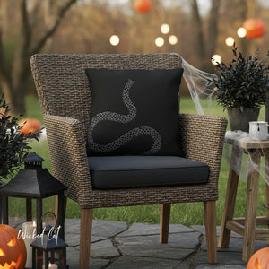 Wicker chair with a black pillow featuring a snake design, surrounded by Halloween decorations outdoors.