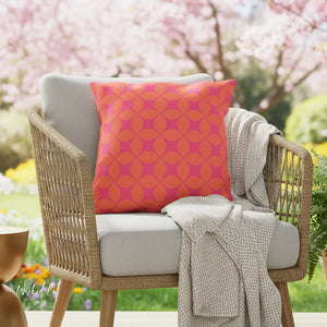 Wicker chair with a pink geometric pillow and beige blanket in an outdoor setting with cherry blossoms.