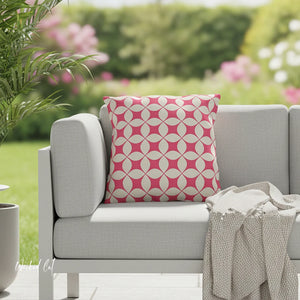 Gray outdoor sofa with a pink and white patterned pillow, surrounded by greenery and flowers.