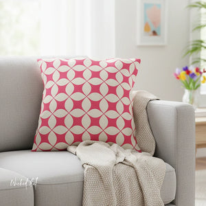 Pink and white patterned pillow on a gray sofa with a neutral blanket, in a bright room.