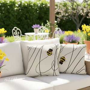 White outdoor sofa with decorative pillows featuring bee designs, set against a garden backdrop.