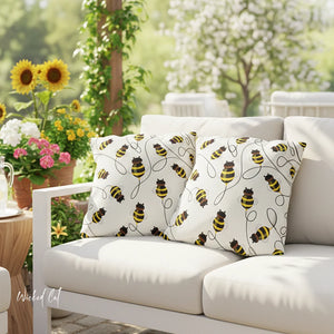 Bees patterned pillows on a white outdoor sofa with sunflowers and flowers in the background.