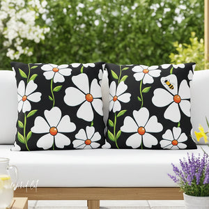 Two decorative pillows with white flowers on a black background on a white couch outdoors.