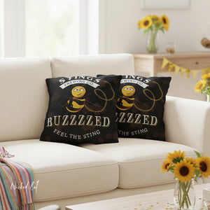 Two decorative pillows with bee designs and text on a beige couch in a living room setting.