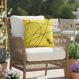 Wicker chair with a yellow pillow featuring a bee design in an outdoor setting.