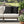 Black decorative pillows with gold patterns on a beige outdoor sofa, surrounded by plants and a fountain.