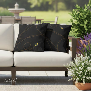 Black decorative pillows with gold patterns on a beige outdoor sofa, surrounded by plants and a fountain.