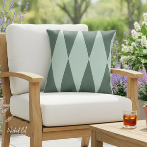 Chair with a green geometric pillow in an outdoor setting with flowers and a glass of iced tea.