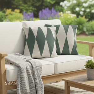 Outdoor sofa with green and white patterned cushions, gray blanket, and small plant in a garden setting.