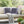 Outdoor setting with a white sofa adorned with purple pillows featuring black floral patterns, a gray blanket, and a small table with a drink.
