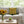 Living room with a gray sofa, green floral pillow, sunflowers in a vase, and apples on a table.