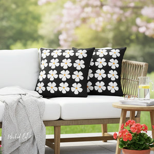 Black pillows with white floral patterns on a white outdoor sofa with a blurred garden background.