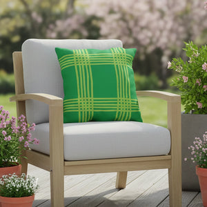 Chair with a green plaid pillow on a wooden deck with plants and flowers in the background