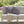 Gray outdoor sofa with striped pink and black cushions and a beige blanket, set against a blurred garden background.