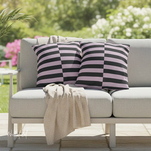 Gray outdoor sofa with striped pink and black cushions and a beige blanket, set against a blurred garden background.