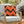 Orange pillow with black zigzag pattern on a chair outdoors with Halloween decorations.