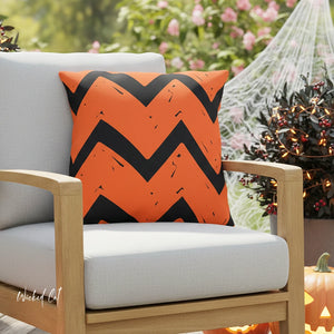 Orange pillow with black zigzag pattern on a chair outdoors with Halloween decorations.