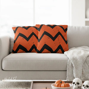 Orange and black chevron patterned pillow on a gray sofa with Halloween decorations in the foreground.