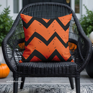 Orange and black chevron patterned pillow on a wicker chair with pumpkins in the background.