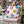 A square decorative throw pillow with a colorful Christmas ornament print, resting on a distressed white metal garden chair in a snowy backyard setting.