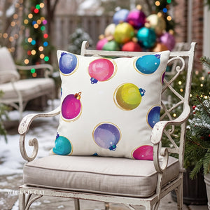 A square decorative throw pillow with a colorful Christmas ornament print, resting on a distressed white metal garden chair in a snowy backyard setting.