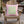 A pink throw pillow with a light green square containing pink candy cane motifs, displayed on a wooden Adirondack chair in an outdoor patio setting.