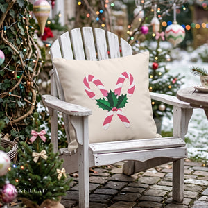 A cream-colored Adirondack-style outdoor chair on a stone patio, featuring a square throw pillow with a pink and green Christmas candy cane and holly design, set against a festive holiday garden background.