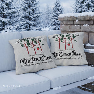Two outdoor pillows that read Woodstocks Christmas Trees on a sofa in a snow covered background.