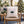 A square cream throw pillow with a Christmas design of two purple-and-white candy canes crossing over green holly leaves, displayed on a woven wooden chair in a cozy, softly blurred living room with a Christmas tree in the background.