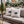 Two beige outdoor throw pillows with a green holly and purple candy cane design, displayed on a beige patio sofa decorated for Christmas.