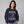 A woman wearing a navy blue crewneck sweatshirt with a graphic of a skeleton sitting cross-legged surrounded by colorful autumn leaves, with the text 'IT'S THE MOST WONDERFUL TIME OF THE YEAR'.