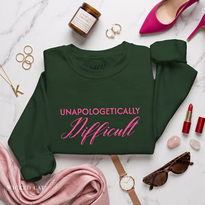 folded green sweatshirt with embroidered pink text 'unapologetically difficult'