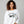Woman wearing a white sweatshirt with 'Love Potion No. 9' text and snake graphic on a gray background.