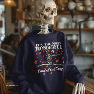 Skeletal figure wearing a navy sweatshirt with Halloween-themed design in a cozy room.