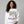 Woman wearing a white sweatshirt with a Christmas tree design and text.