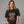Woman wearing a black t-shirt with 'Sleepy Hollow Enchanted Orchards' design on a gray background