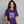 Woman wearing a purple t-shirt with white graphic design and text Witch Please on a gray background