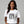 Woman wearing a white t-shirt with black graphic design and text on a gray background