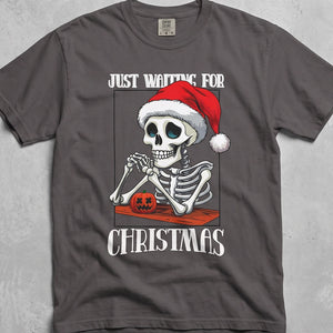 Grey t-shirt with graphic of skeleton wearing a Santa Hat and text 'Just Waiting for Christmas'