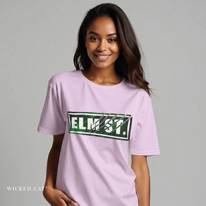 Woman wearing a light purple t-shirt with 'ELM ST.' printed on it against a gray background