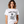 Woman wearing a white t-shirt with a graphic of a skeleton holding a martini with Bone-Jour in bone style lettering at the top.