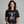 Woman wearing a black t-shirt with a graphic of a skeleton holding a martini with Bone-Jour in bone style lettering at the top.